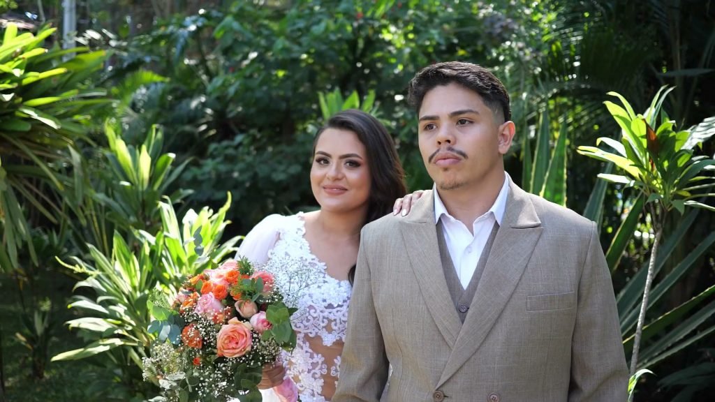 Noiva e noivo se olhando de perto, com o buquê de flores laranja em primeiro plano