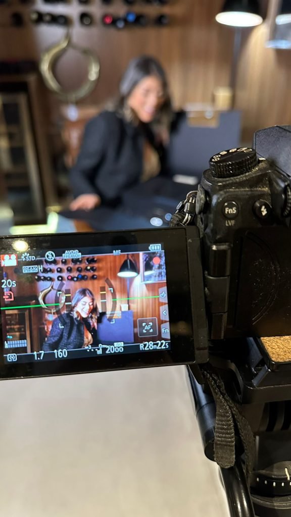 Monitor de câmera em primeiro plano enquadrando uma entrevista em ambiente interno, com a entrevistada sentada ao fundo