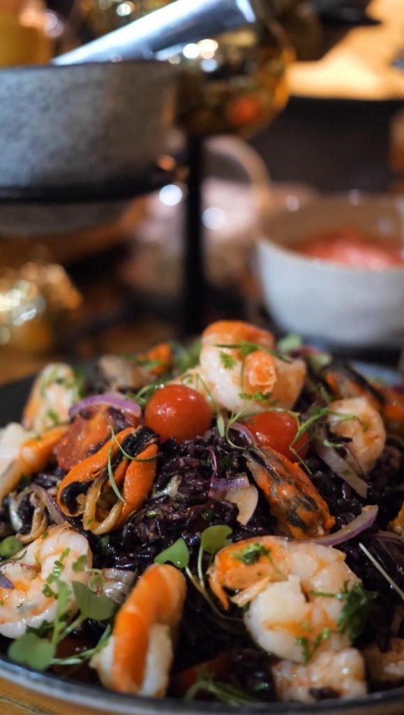 Prato de frutos do mar com camarão, tomate e ervas visto de cima, em mesa escura, gravado para vídeo institucional de gastronomia
