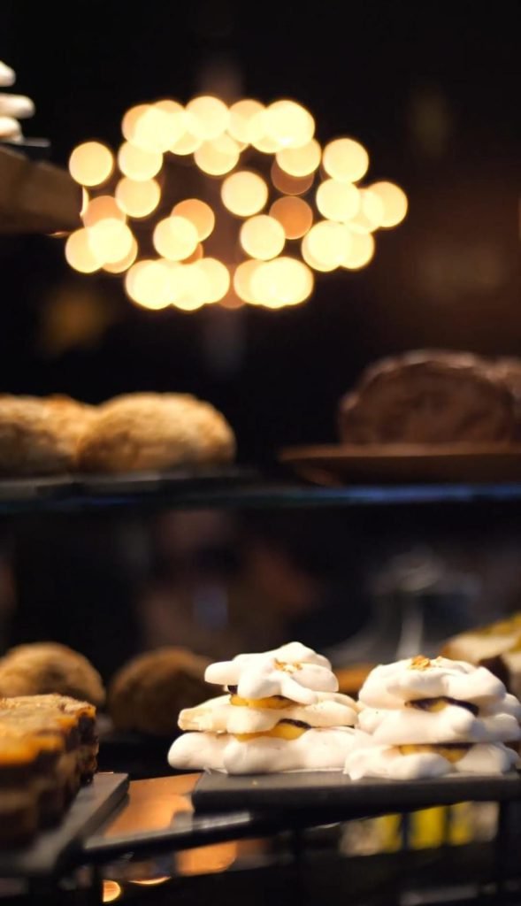 Vitrine iluminada com pães artesanais e doces em bandejas escuras, gravada para vídeo institucional de gastronomia