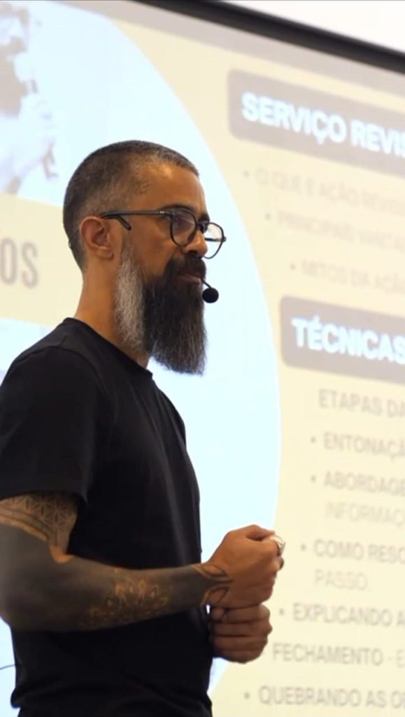 Palestrante de camiseta preta falando ao lado da projeção com os tópicos da apresentação, durante gravação de teaser de evento