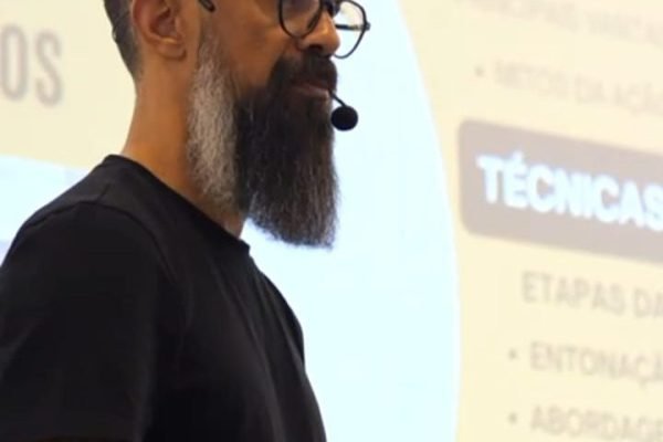Palestrante de camiseta preta falando ao lado da projeção com os tópicos da apresentação, durante gravação de teaser de evento